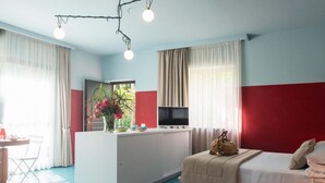 A compact hotel room with a kitchenette, a bed, a desk with a chair, and a TV.