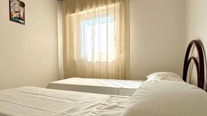 A room with two beds, a window with sheer curtains, and a wooden headboard. - RS324 - Marcelli, seafront three-room apartment with beach included (Marcelli)