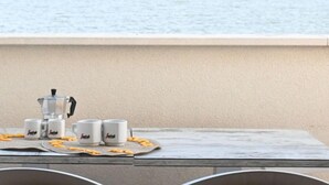 Ett bord med en kaffebryggare, fyra muggar och några snacks, placerat vid en plats med utsikt över havet.