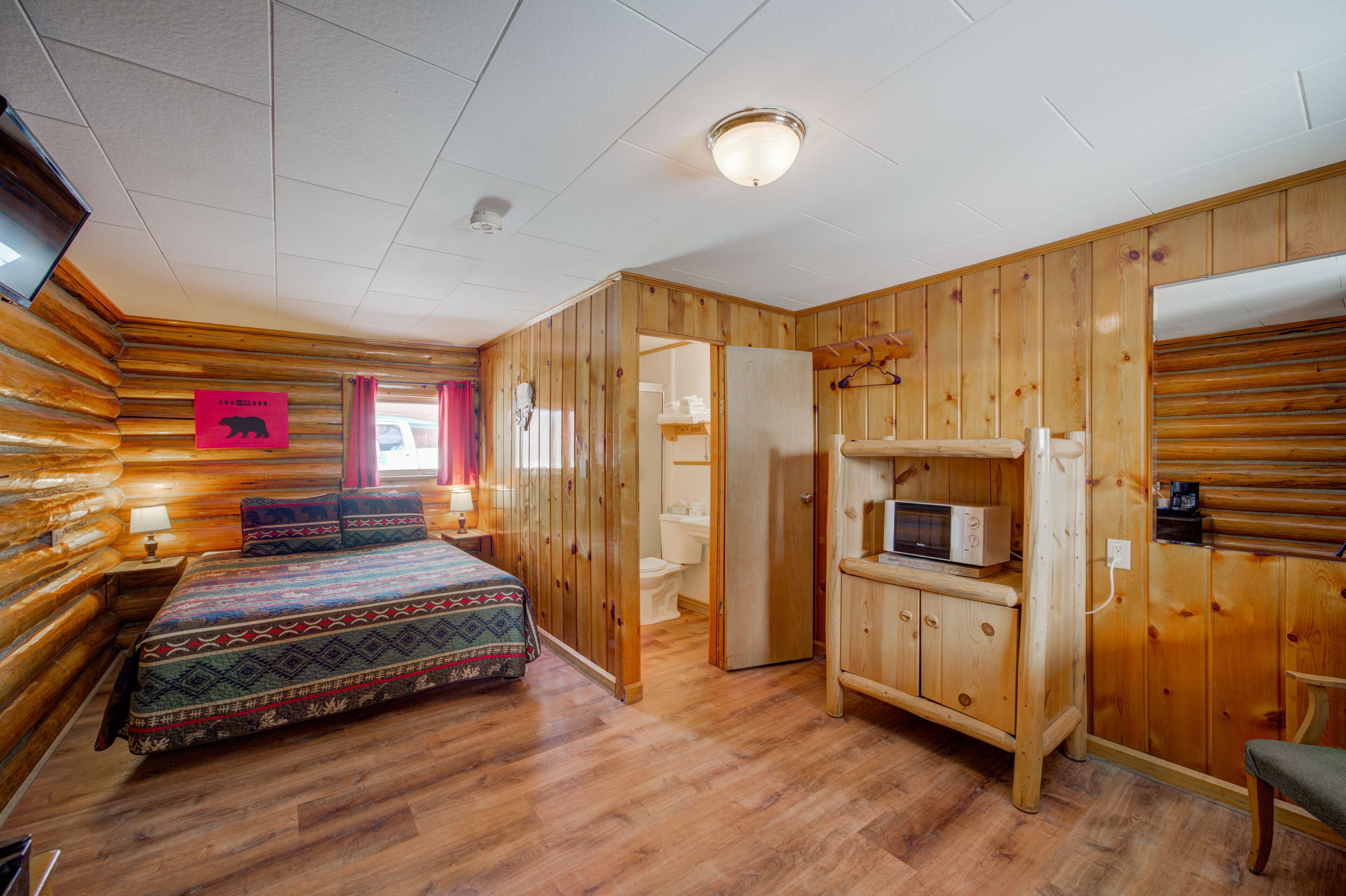 Una habitación tipo cabaña de madera con una cama, un microondas y un televisor.