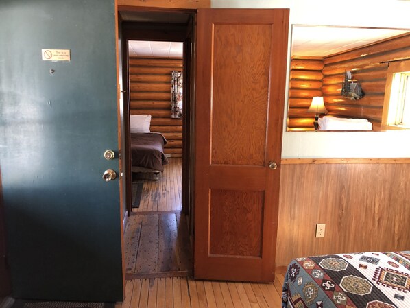 A wooden cabin interior with a bed, a small desk with a lamp, and a sign indicating a non-smoking room.