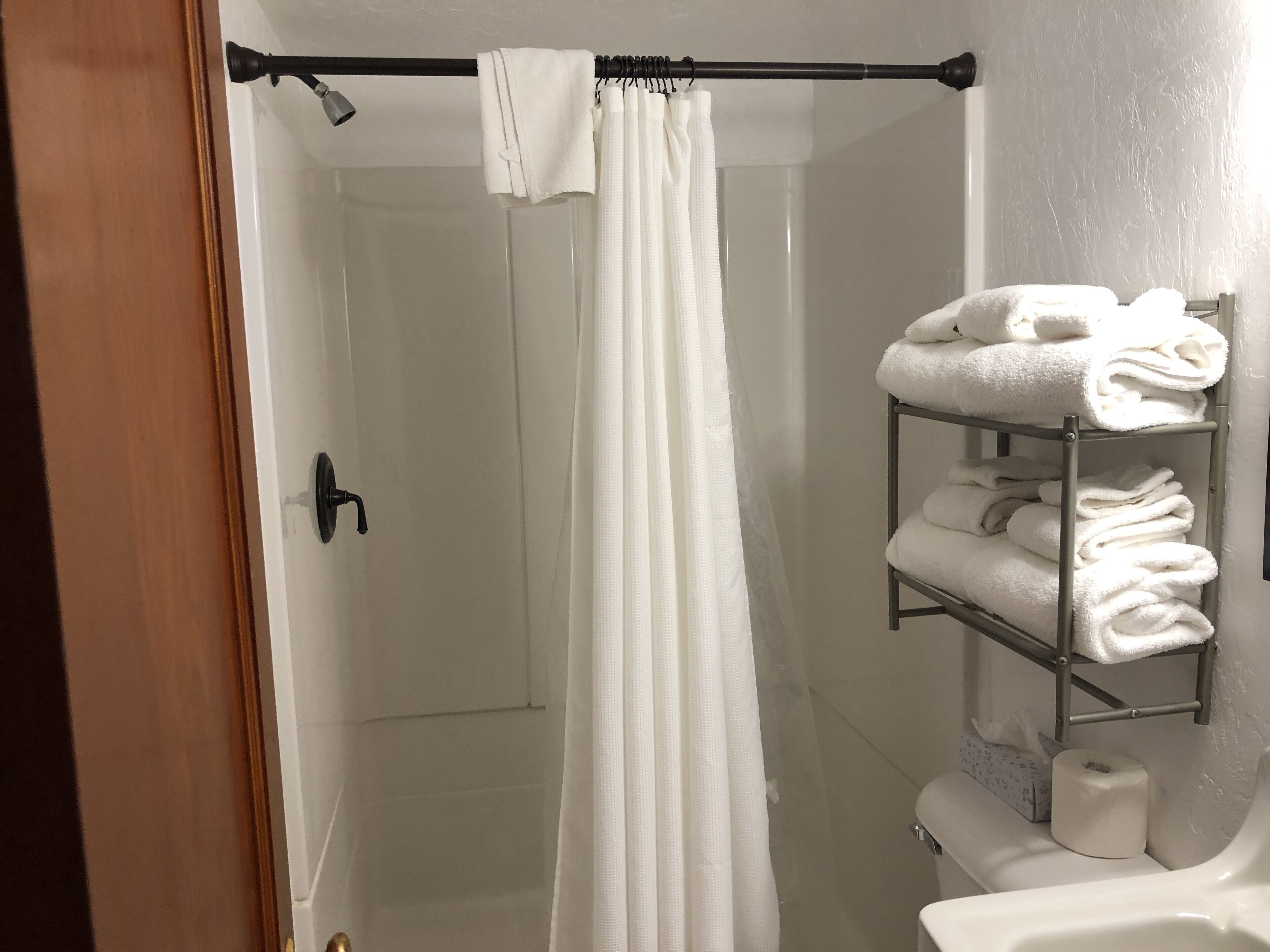 Un baño con ducha, un perchero con toallas y un inodoro.
