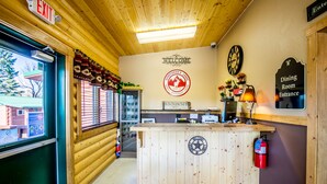 A wooden interior with a reception desk, a clock, and a sign indicating the dining room entrance. - Sportsmans Lodge (Ennis)