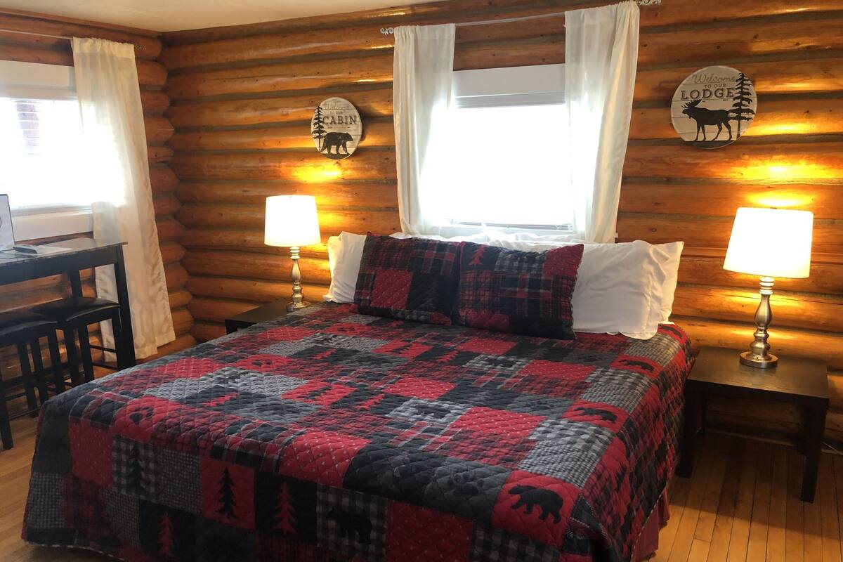 A log cabin room with a bed, two nightstands with lamps, a desk, and a chair.
