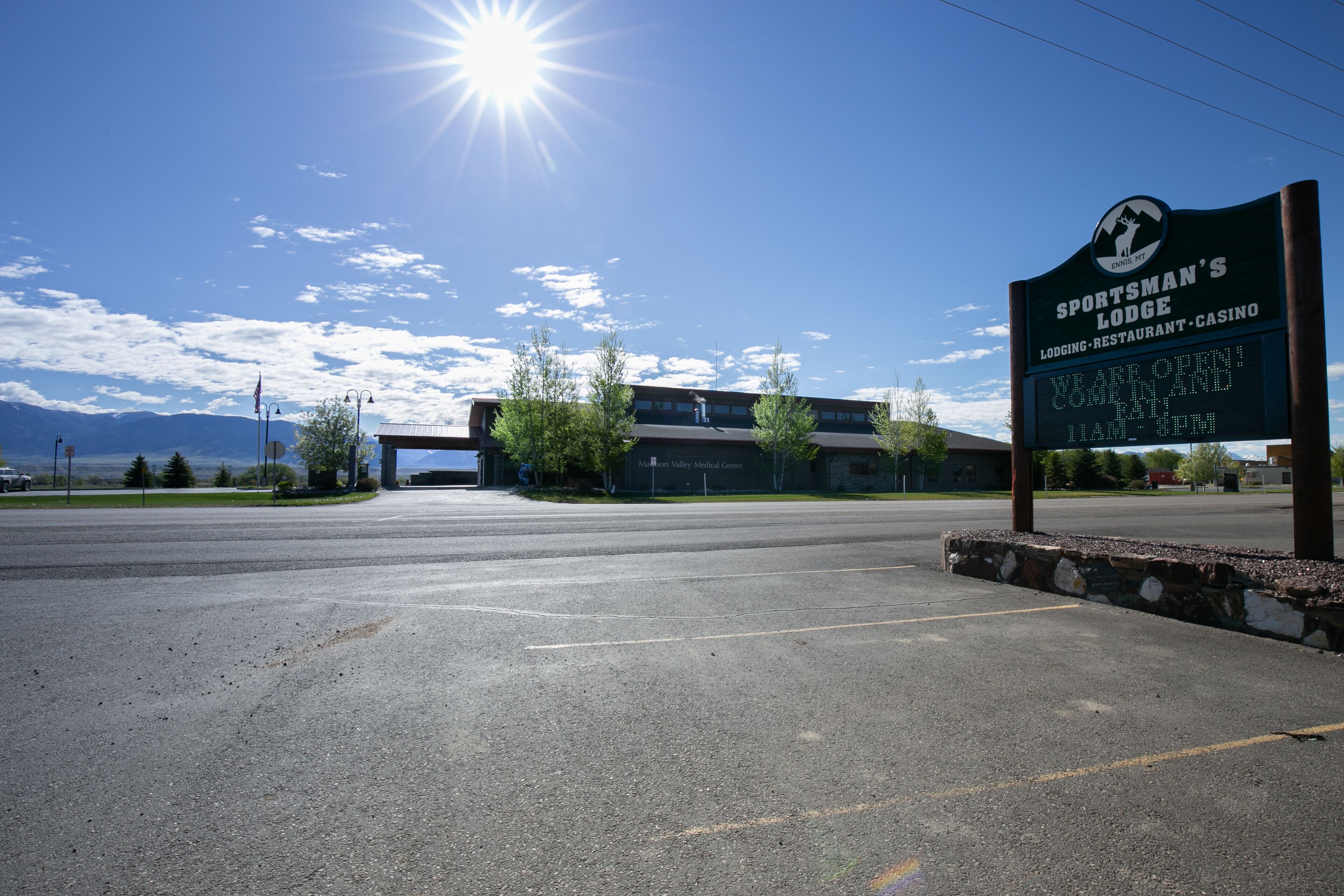 A parking lot with a sign for Sportsman's Lodge, featuring a mountain view and a clear sky.