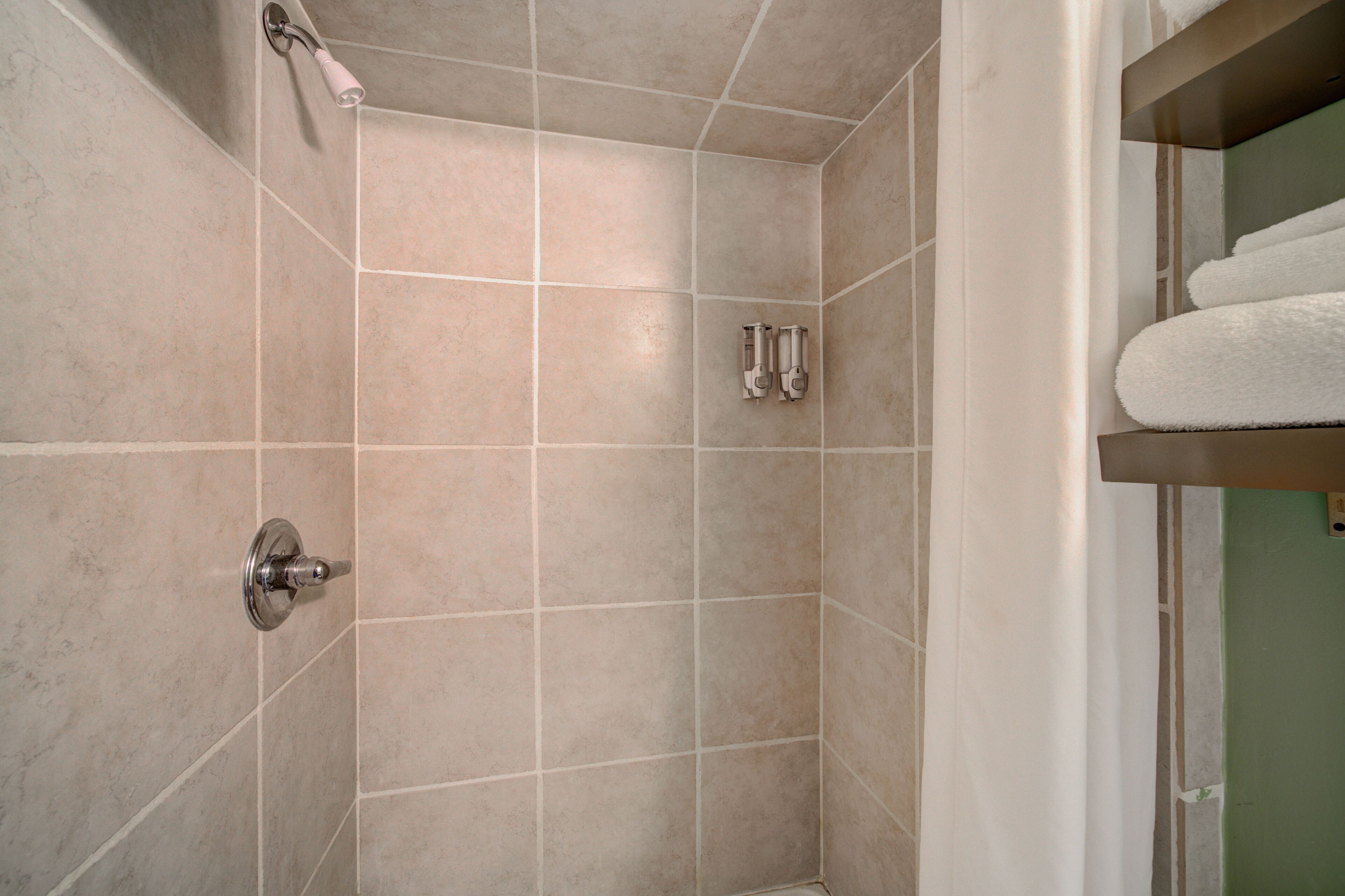 A bathroom with beige tiles, a shower with a handheld showerhead, and a towel rack with towels.