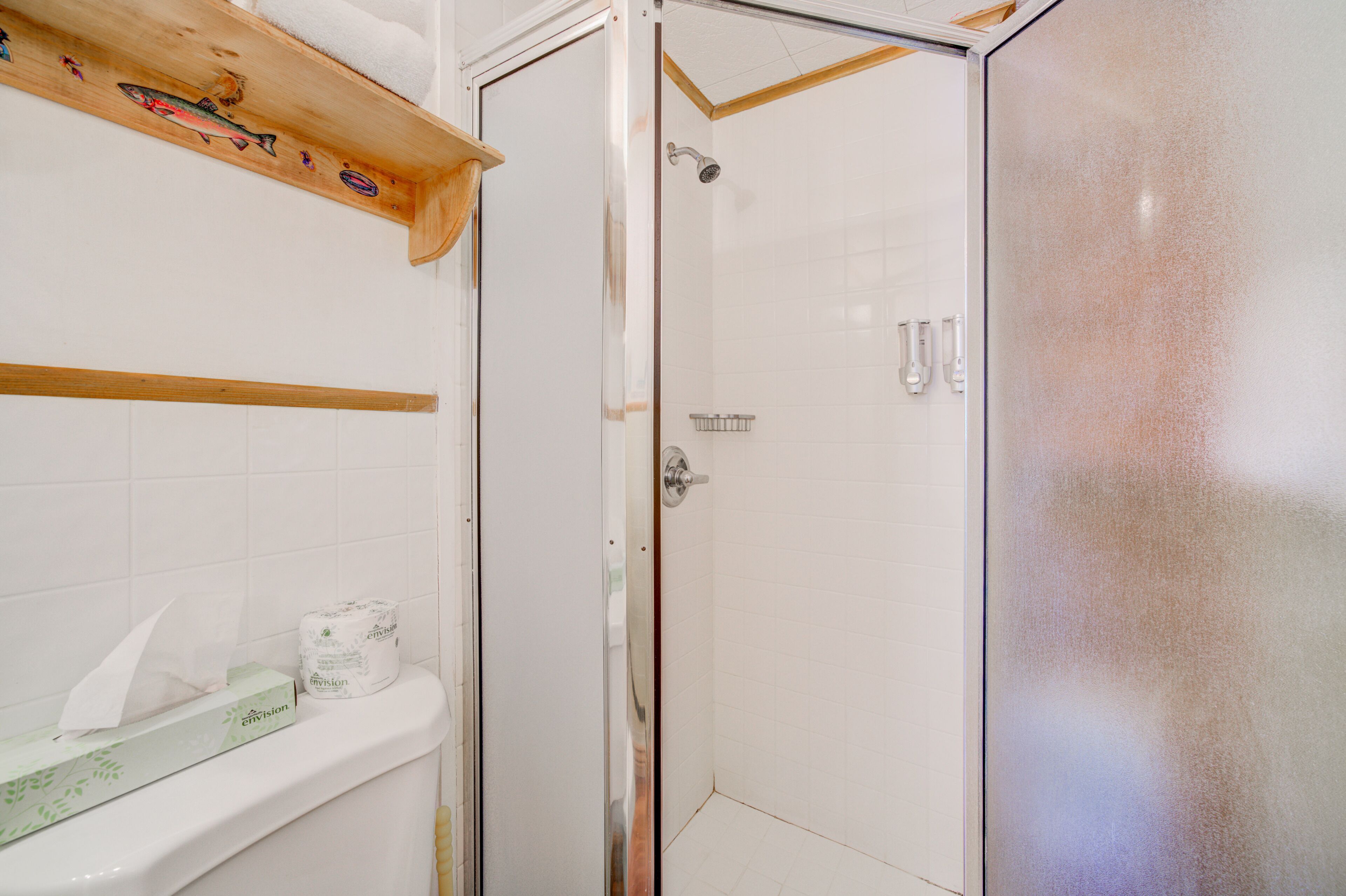 Une salle de bain avec une douche, des toilettes et une étagère décorée d’un motif de poisson.