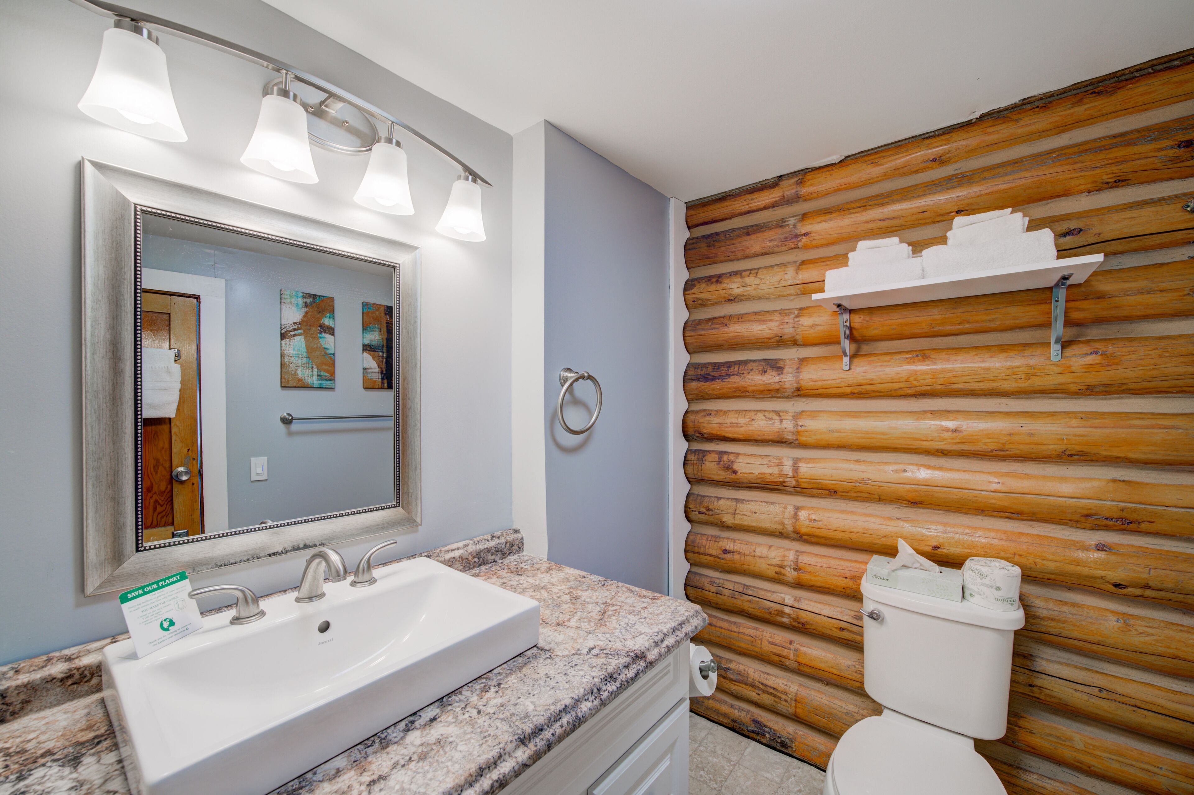 A bathroom with a granite countertop sink, a large mirror, and a wooden log wall.