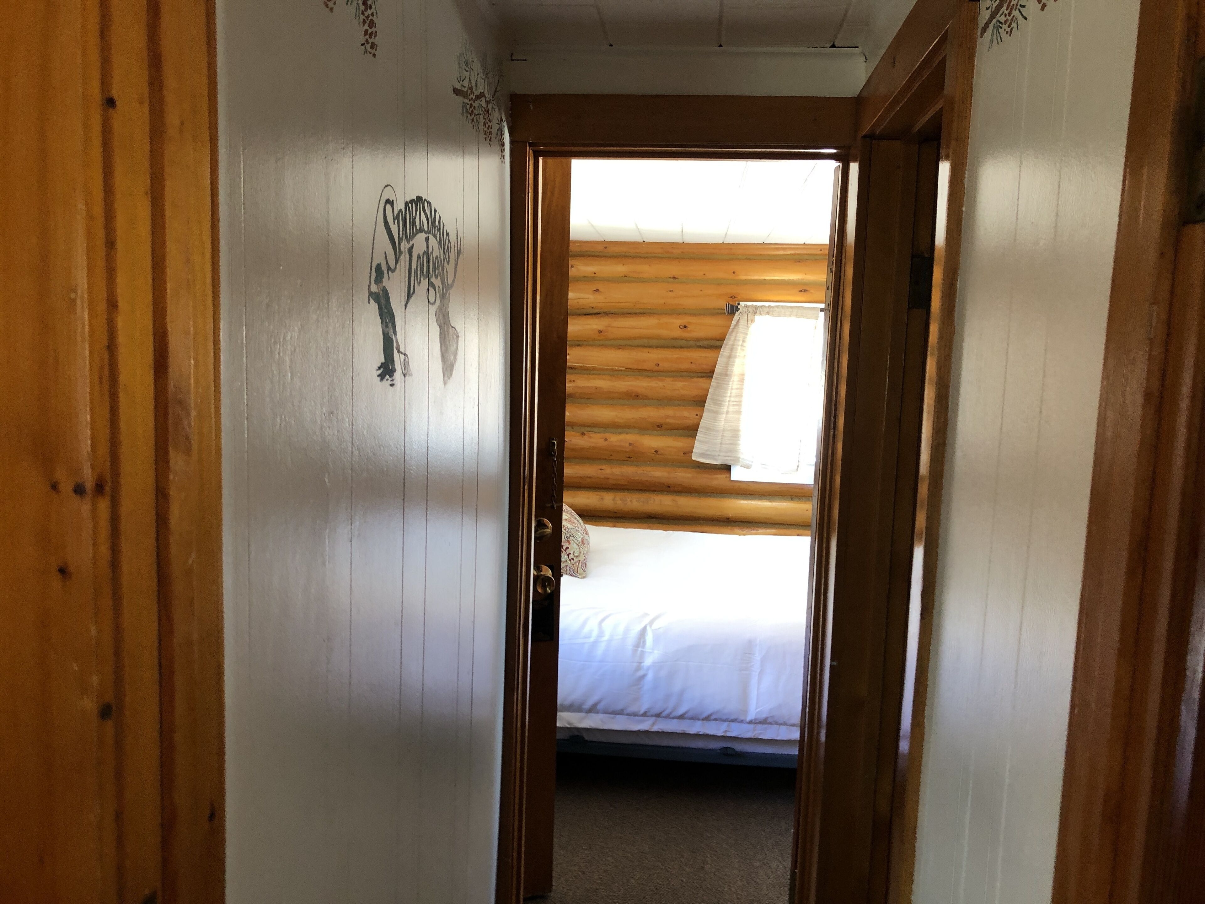 Un couloir étroit aux murs en bois, avec une porte donnant sur une chambre à coucher équipée d’un lit et d’une fenêtre.