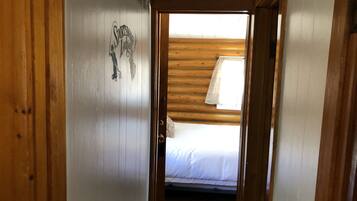 Un couloir étroit aux murs en bois, avec une porte donnant sur une chambre à coucher équipée d’un lit et d’une fenêtre.