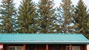A log cabin with a green roof, two windows, and two Adirondack chairs outside. - Sportsmans Lodge (Ennis)