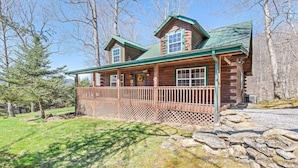 A log cabin with a porch, a stone wall, and a forested backdrop.