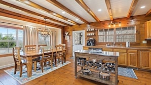 A wooden interior with a dining table, chairs, a kitchen with wooden cabinets, and a window with a view.