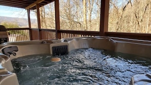 A hot tub with a wooden deck and a view of trees.