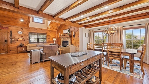A rustic interior with wooden beams, a fireplace, a dining table, and a sofa.