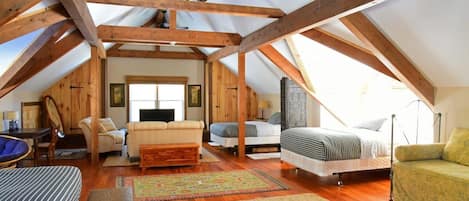 A spacious attic bedroom with exposed wooden beams, a large bed, a sofa, and a chair.