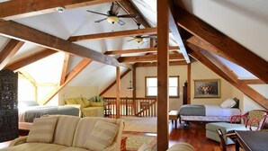 Un'ampia camera da letto in mansarda con travi a vista, soffitto inclinato e un'ampia finestra. Si trova un letto, un divano e un tavolo da pranzo.