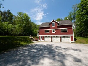 Une maison rouge à deux étages, dotée d’un garage, entourée d’une pelouse bien entretenue et d’arbres.
