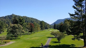 Un campo de golf con un camino despejado, rodeado de árboles y colinas.
