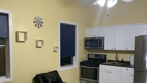 Un espace de vie compact comprenant un coin cuisine, un ventilateur de plafond, un jeu de fléchettes et une fenêtre avec un store.