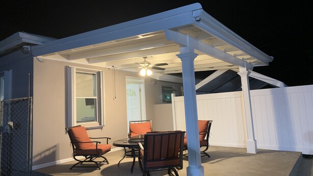 Un patio couvert avec un ventilateur de plafond, une table et quatre chaises.