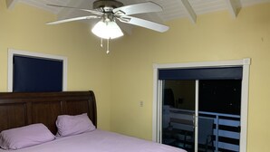 Une chambre à coucher avec un lit, un ventilateur de plafond, une fenêtre donnant sur l’extérieur et une porte.