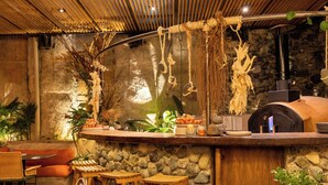 Eine rustikale Bar mit Steinwand, Holzstühlen, einem Pizzaofen und verschiedenen Barkellen.