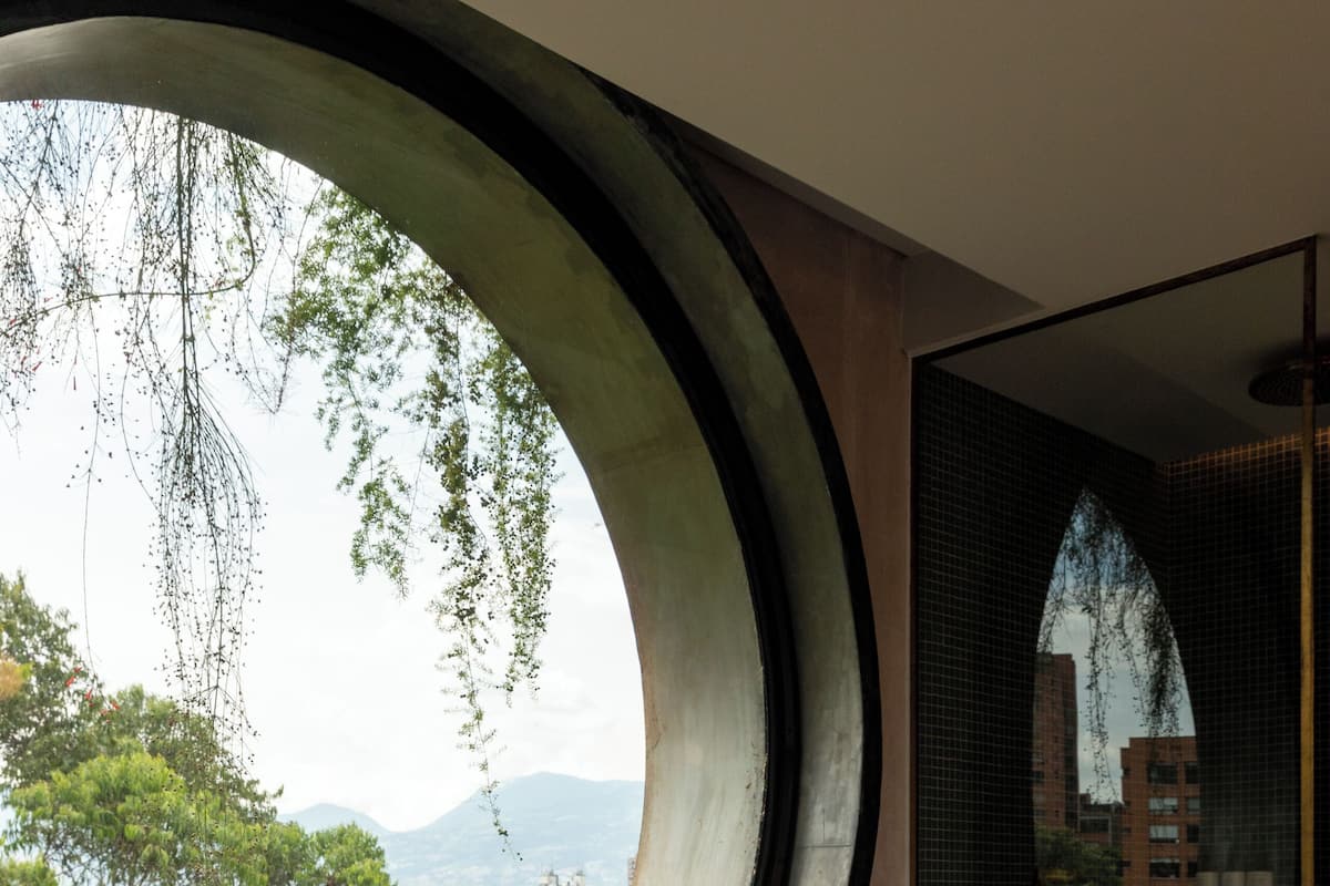 A modern bathroom with a freestanding bathtub, large circular windows, and a view of the cityscape.