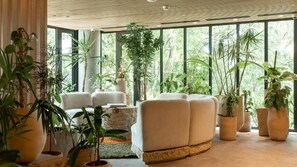 Een modern interieur met grote ramen, een bank en diverse potplanten.