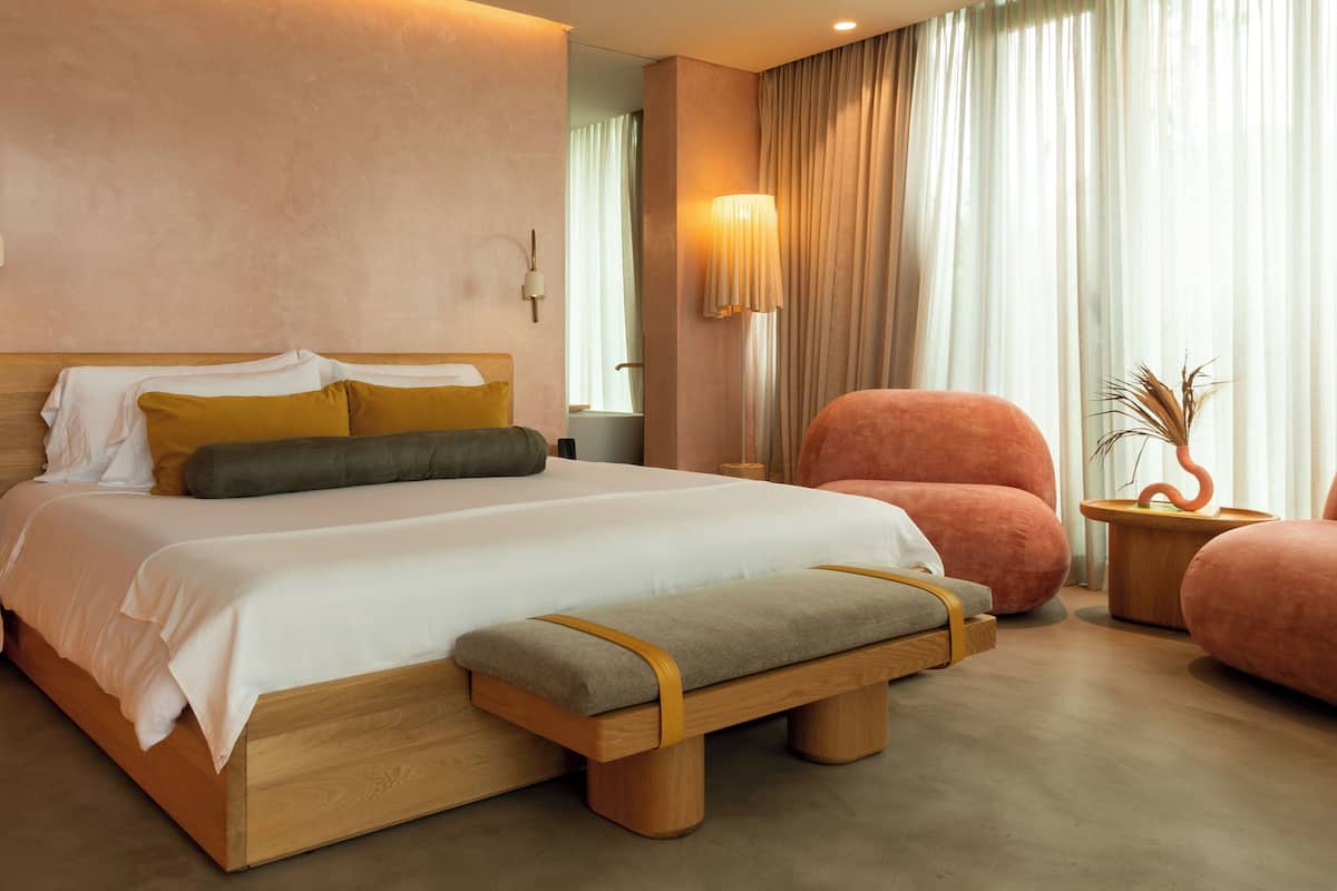 A modern bedroom with a wooden bed, a bench, a chair, and a nightstand with a vase.