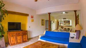 Una sala de estar con un sofá, televisor, mueble de madera y una planta.