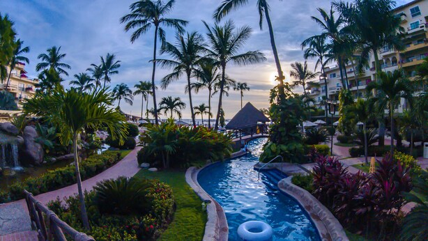 Un resort con piscina, palmeras y vistas al océano.