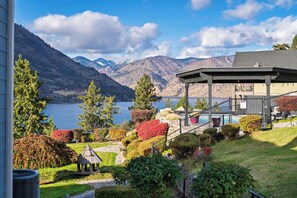 Vista sobre un lago con un pabellón, un jardín cuidado y montañas al fondo.