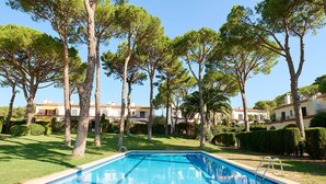 A swimming pool surrounded by tall trees and well-maintained lawns, with buildings in the background.