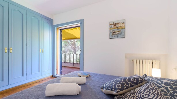 Un dormitorio con cama, un armario azul, una puerta que da a un balcón exterior y un radiador fijado a la pared.