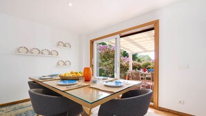 A dining area with a glass table, grey chairs, and a fruit bowl.