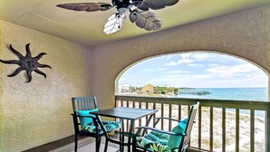 Un balcon avec vue sur l’océan, un ventilateur de plafond et une table avec des chaises.