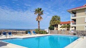 Une piscine rectangulaire à l’eau d’un bleu limpide, entourée d’une clôture en bois et de chaises longues bleues.