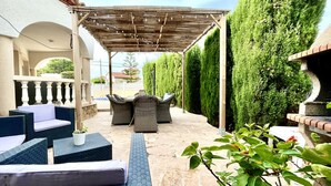 Un espace extérieur aménagé en terrasse, doté d’une pergola, de coins salon et de haies soigneusement taillées.