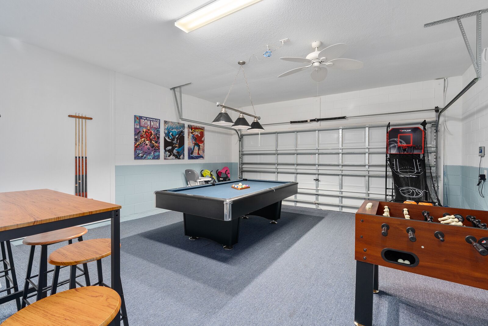 A room with a pool table, a foosball table, and a ceiling fan.