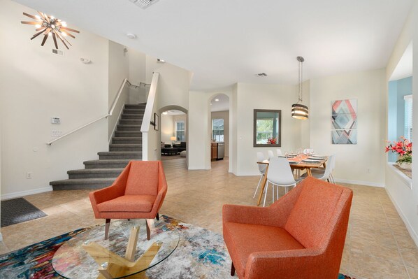 A spacious living area with a staircase, a dining table set for six, and a modern chandelier. - Spacious Family Villa, Game Room, Minutes from Disney, Universal & Shops (Kissimmee)