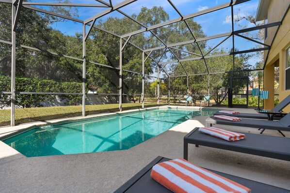 A swimming pool with a glass enclosure, surrounded by lounge chairs and a covered patio area.