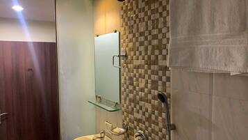 A bathroom with a wooden door, a glass shelf above a sink, a mirror, and a shower with a checkered tile wall.