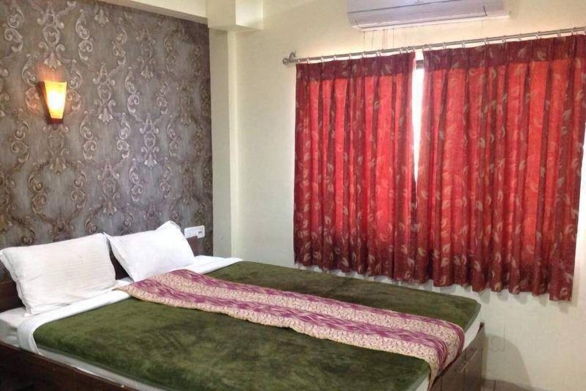 A bedroom with a bed, a wall-mounted light, and a window with red curtains.
