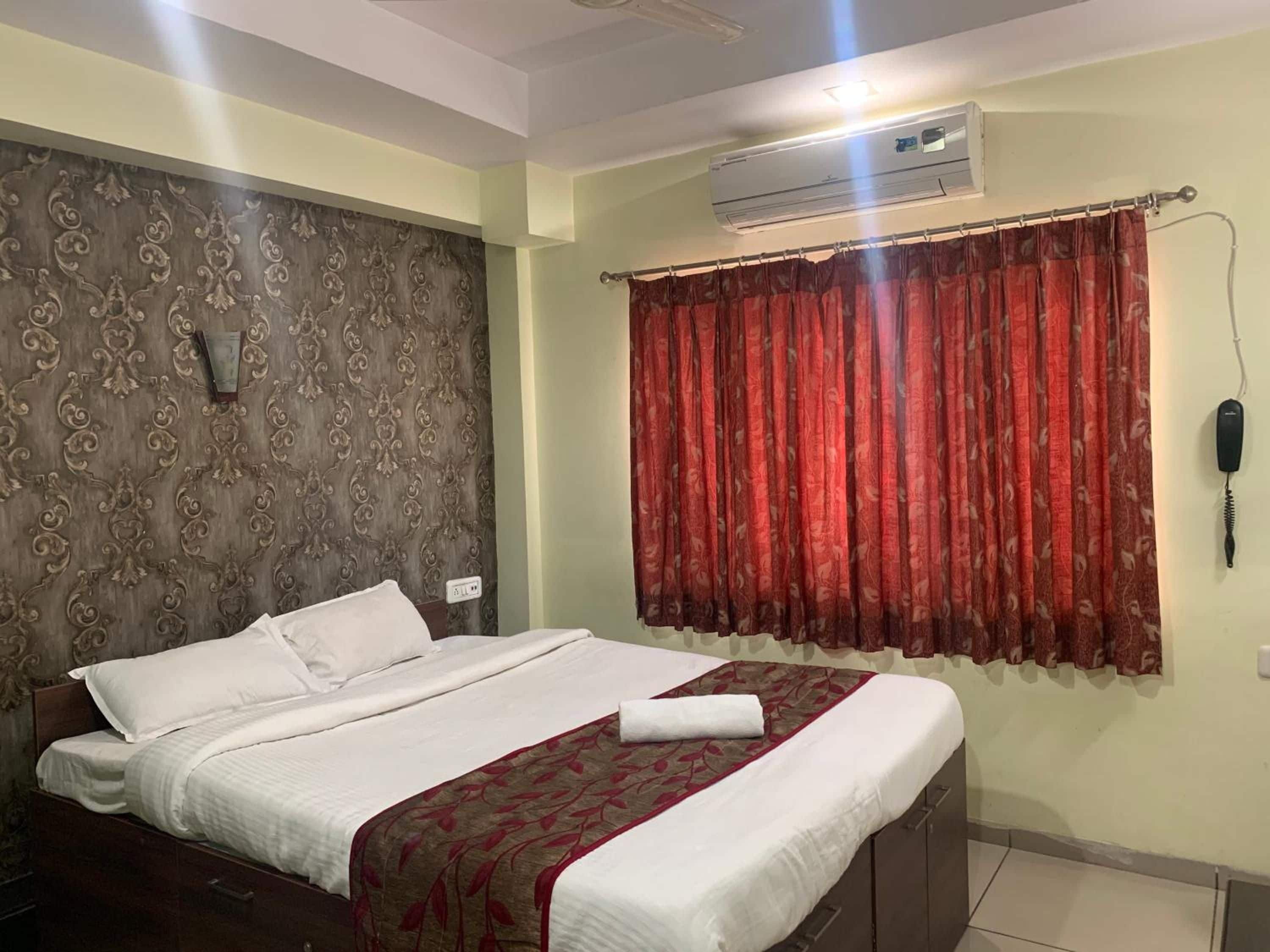 A hotel room with a bed, an air conditioning unit, a telephone, and a curtain.