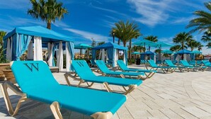 Un área junto a la piscina con hileras de sillones azules y toldos azules.