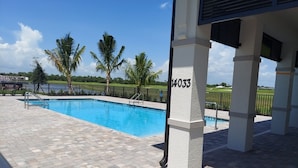 A swimming pool with a paved deck, palm trees, and a clear sky. - New condo at golf & country club overlooking preserve and course (Punta Gorda)