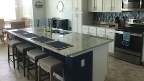 A modern kitchen with a large island, stainless steel appliances, and a tiled backsplash. - New condo at golf & country club overlooking preserve and course (Punta Gorda)