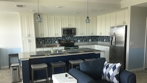 A modern kitchen with white cabinets, a central island with stools, a refrigerator, and pendant lighting. - New condo at golf & country club overlooking preserve and course (Punta Gorda)