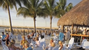 A beachside restaurant with outdoor seating, palm trees, and a thatched roof structure. - New condo at golf & country club overlooking preserve and course (Punta Gorda)